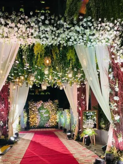 An enchanting nighttime entrance where the aisle is flanked by a canopy of white flowers and hanging greenery. The soft glow from the lights creates a magical, forest-like atmosphere that feels intimate and romantic.