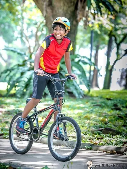 A big smile from a boy on his bicycle in the park. This is a great example of a lifestyle kids photoshoot, capturing them doing what they love in a natural setting.