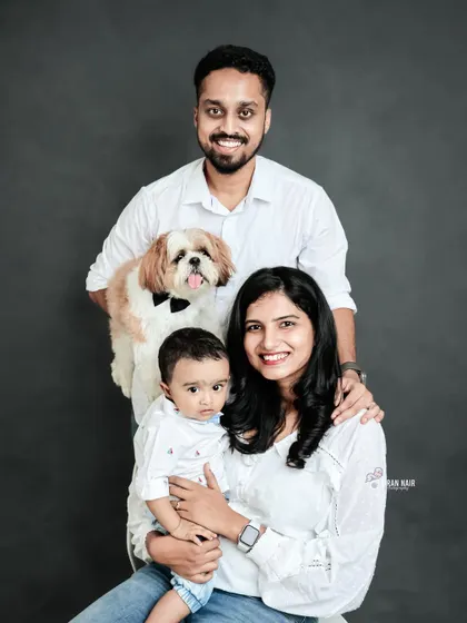 A formal studio portrait of a family, including their pet dog wearing a bow tie. This image is a great example of a classic family photo that includes every member.