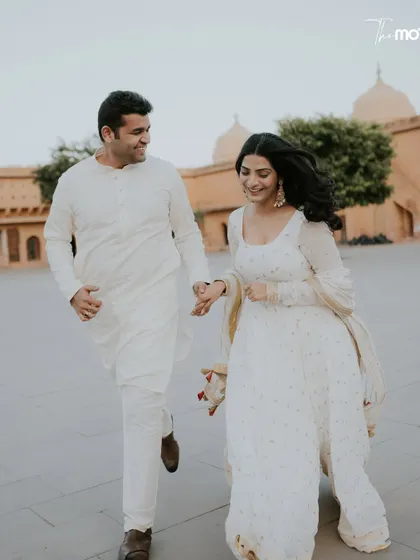 A playful, candid moment of the couple running and laughing in a Jaipur palace courtyard. Their all-white outfits and genuine smiles create a fresh, joyful, and authentic pre-wedding photograph.
