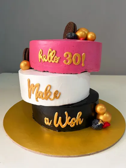 "Hello 30!" This modern, asymmetrical cake uses bold blocks of pink, white, and black for a striking design. It's a chocolate truffle cake perfect for a stylish 30th birthday celebration.