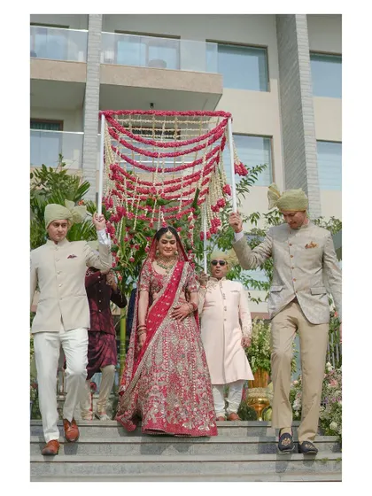 The bride makes her grand entrance, escorted by her brothers under a 'phoolon ki chadar' (floral canopy). This shot captures a classic and emotional Indian wedding tradition.