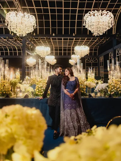 A quiet moment for the couple amidst the grandeur of their reception. The deep blue decor, crystal chandeliers, and endless candles create a cinematic and romantic atmosphere, perfectly captured in this portrait.