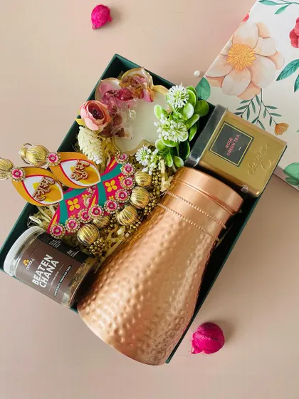 This hamper, presented in a box with a beautiful floral lid, includes a hammered copper bottle, Beaten Chana snack, and decorative hangings.