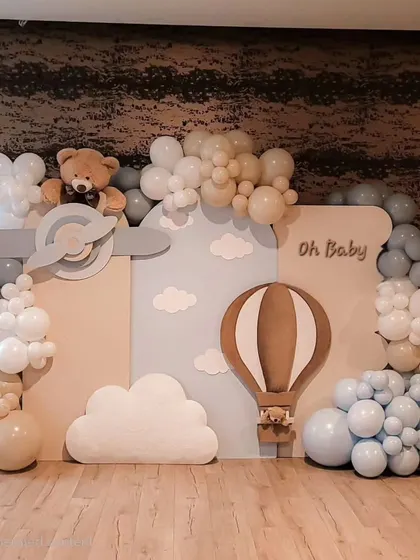 An "Oh Baby" setup with a hot air balloon and airplane theme. The backdrop creates a sky full of clouds made from balloons, with wooden cutouts of a plane and hot air balloon for a vintage adventure feel.