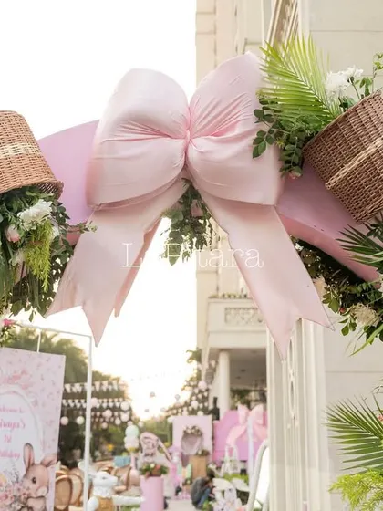 A close-up of the pink entrance arch, topped with a large bow and adorned with flowers spilling out of wicker baskets.