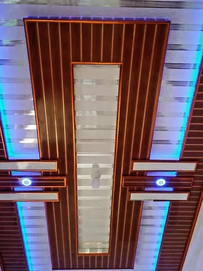 A bold, symmetrical PVC ceiling design with a dark wood finish. The bright blue side lighting creates a striking contrast and a very modern feel.