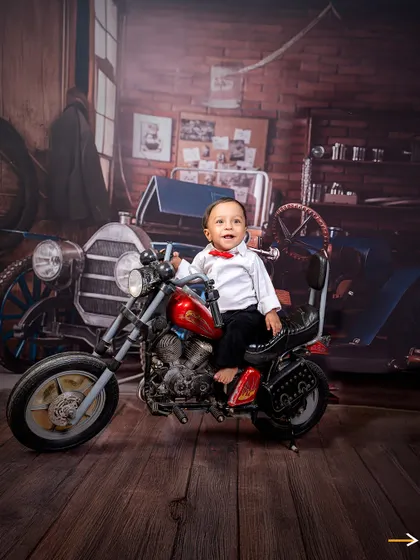 A classic biker pose. This little boy sits confidently on his mini motorcycle, with a bright smile and a sharp red bow tie.