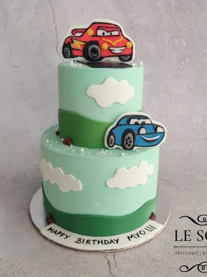 A two-tier cake for a fan of the movie Cars. This 2 kg Chocolate Truffle cake features 2D fondant figures of Lightning McQueen and Sally against a backdrop of rolling green hills.