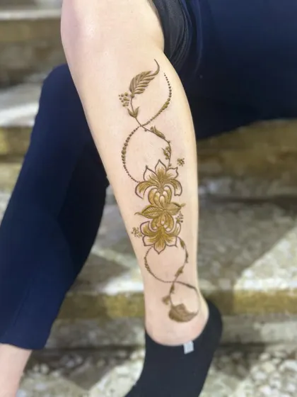 An elegant vine design that wraps around the leg in an infinity loop. This infinity henna tattoo style incorporates delicate flowers and feathers for a modern and symbolic look.