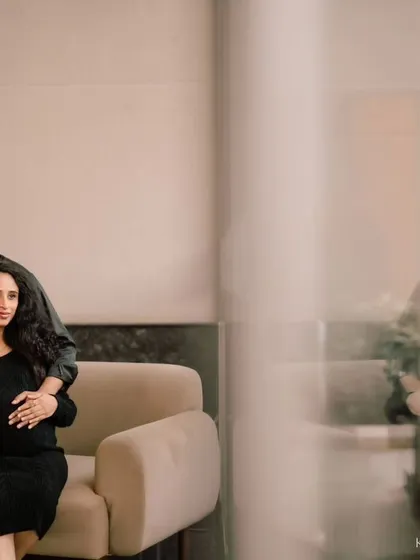 A modern, chic indoor maternity portrait. The couple's coordinated black outfits and the clean, minimalist setting create a sophisticated and timeless look.