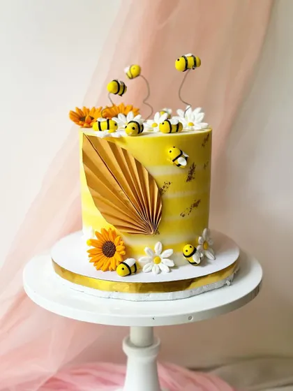 A full view of the bee and sunflower cake, showing the golden paper fan detail that adds a modern touch to the design.