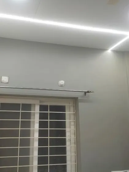 This room features a modern look with cool grey walls and a false ceiling with integrated strip lighting. Our team ensures a flawless finish on both walls and ceilings for a cohesive and polished appearance.
