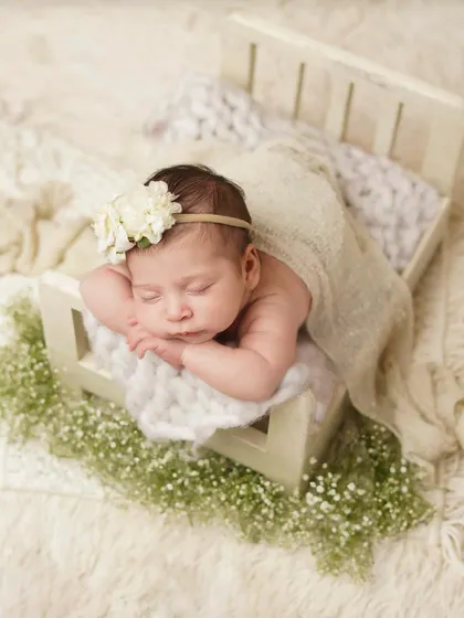 This newborn is nestled in a tiny bed, surrounded by baby's breath. The natural textures and soft lighting create a serene and organic feel for this baby portrait.