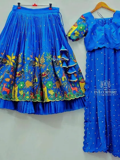 A royal blue lehenga with a hand-painted border. The skirt features a vibrant, artistic painting of a village scene, paired with a simple blue blouse and dupatta.