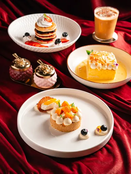 A spread of desserts and a coffee drink at Amelia, set against a luxurious red backdrop. This image conveys a sense of premium indulgence.