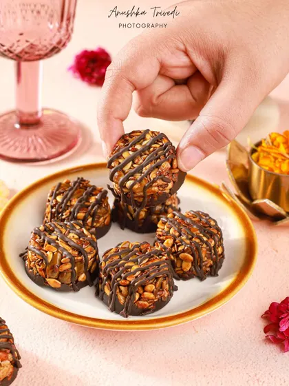 A lifestyle shot of a hand picking up a chocolate-drizzled nut cluster, making the treat look interactive and delicious.
