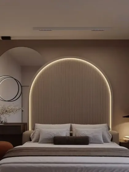 We used curved forms and soft lighting to create a gentle, soothing atmosphere in this bedroom. The arched headboard is complemented by a circular mirror and modern lighting, all in a calming neutral palette.