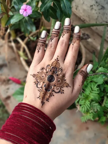 A striking mandala design on the back of the hand. The dark center and intricate surrounding patterns create a beautiful star-like effect.