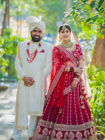 A classic portrait of a Sindhi couple in their wedding attire, standing together in a sunlit garden.