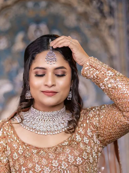 A close-up of a model adjusting her maang tikka. The CZ choker and tikka set is a popular choice for receptions and engagement parties.