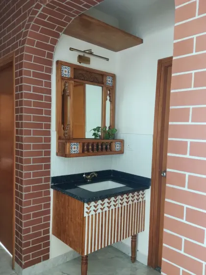 A jharokha-inspired mirror and vanity set in a washbasin area, framed by exposed brick walls. The design incorporates traditional elements like carved details, miniature balusters, and hand-painted tiles.