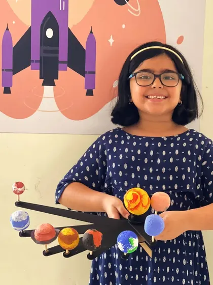 A smiling student shows off her completed solar system model, a project that's both educational and fun.