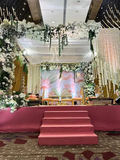 A straight-on view of the mandap stage. The balance of the grand floral structure with the delicate, painted backdrop and simple seating creates a look of sophisticated elegance.