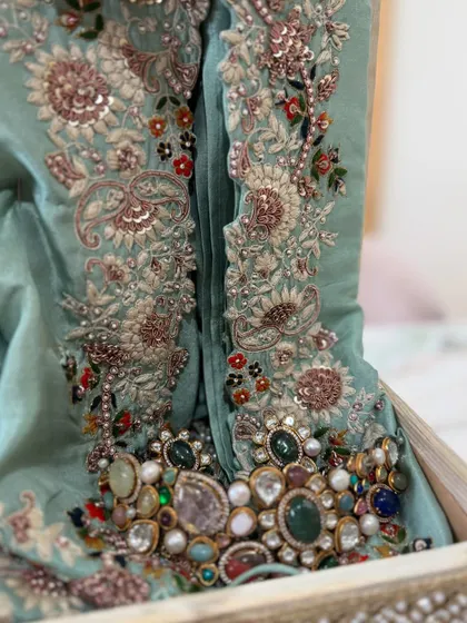 A close-up of the intricate, multi-colored embroidery and beadwork on a mint green outfit, paired with a statement necklace.