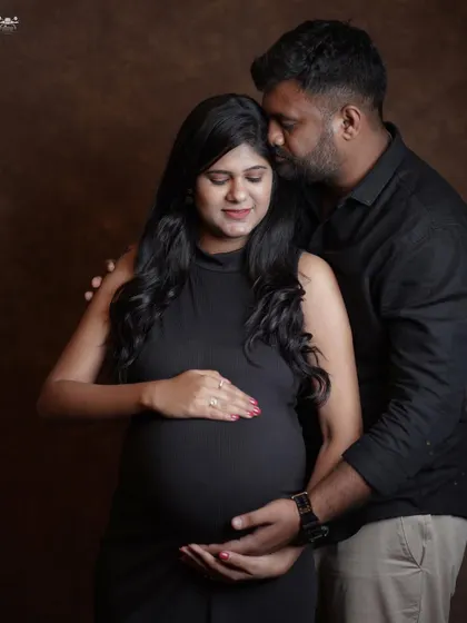 A classic couple's pose against a dark studio backdrop. The focus is entirely on the couple and the baby bump they are lovingly holding together.