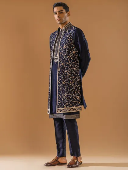 A masterful fusion of tradition and contemporary style, this layered Indo-Western ensemble in midnight blue is a statement of modern luxury. The long, exquisitely embroidered jacket over a classic kurta creates a dynamic silhouette for a sangeet or reception.