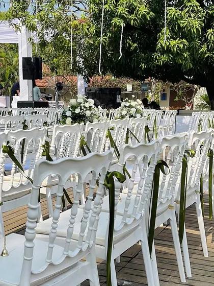 Clean and classic seating for an outdoor wedding. White tiffany chairs are adorned with simple green ribbons, adding a touch of color while maintaining the elegant and fresh aesthetic of the decor.