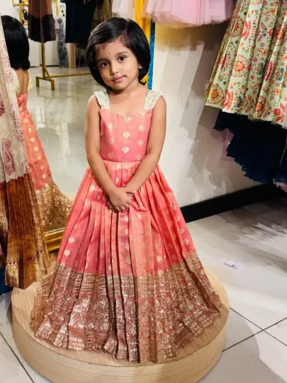 The final look, ready for any celebration. This custom-made peach brocade dress combines traditional fabric with a modern frock silhouette, making it a versatile and stylish choice for any kid's wardrobe.