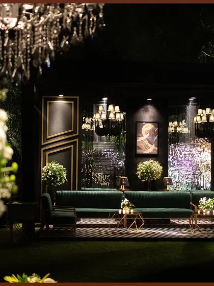 A lounge setup for a cocktail night, featuring deep green velvet sofas against a modern, geometric backdrop. The lighting and floral arrangements add softness to the contemporary design.