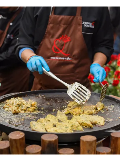 A chef preparing marinated chicken on a large flat-top tawa grill, a versatile station for cooking a variety of Indian appetizers and mains.