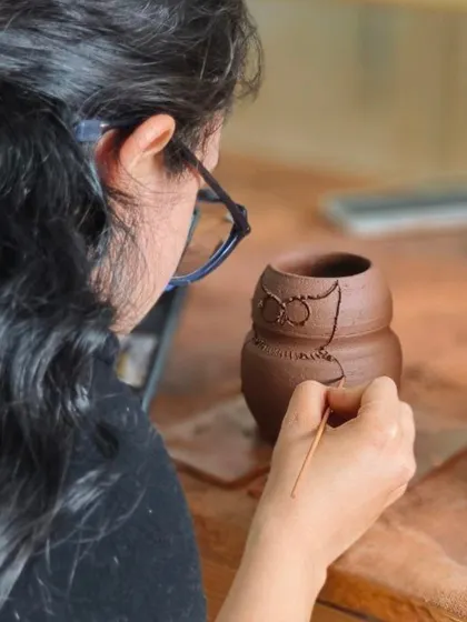 An artist carefully carves the details of an owl onto a wheel-thrown pot. This shows how hand-sculpting techniques can be combined with wheel work to create unique designs.