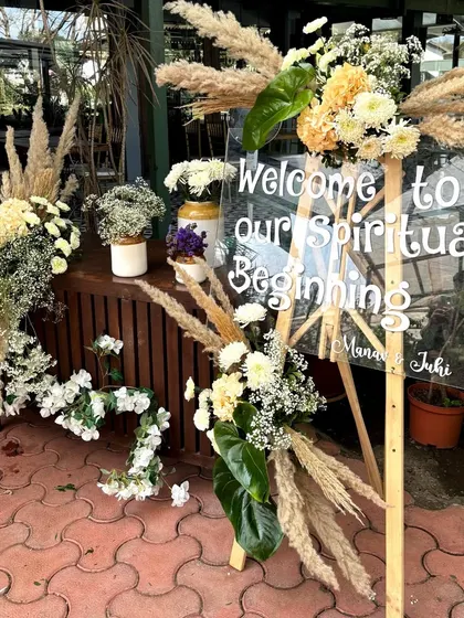 A welcome sign for a "Spiritual Beginning," combining a modern acrylic sign with rustic pampas grass and white floral arrangements.