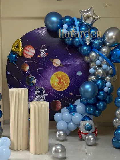 An out-of-this-world space theme for a 4th birthday. This features a galaxy backdrop, a silver and blue balloon garland, and astronaut cutouts.