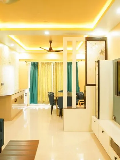 A spacious living room with textured yellow walls and a modern TV unit that acts as a partition. The peripheral ceiling lights create a warm and inviting glow.