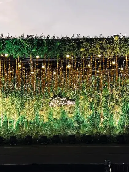 A stunning reception stage with a lush green wall of foliage and hanging golden strings, creating a magical forest vibe.