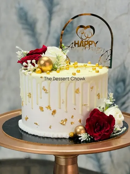 An elegant white drip cake decorated with red and white roses and gold leaf flakes. This tall cake is perfect for an anniversary or a special birthday.