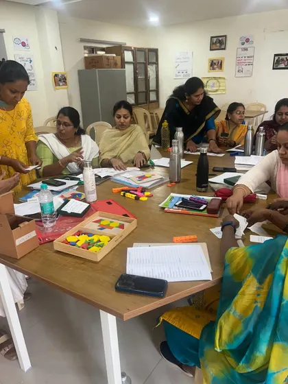 Teachers gathered around a table filled with colorful manipulatives like pattern blocks and cards. This is where theory becomes practice, as they explore different ways to teach math concepts visually.