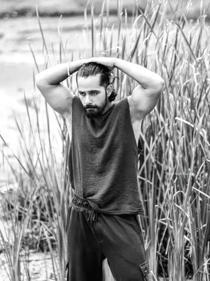 A black and white portrait of an actor in a natural, outdoor setting. The focus is on his strong physique and intense expression, creating a raw and powerful image.
