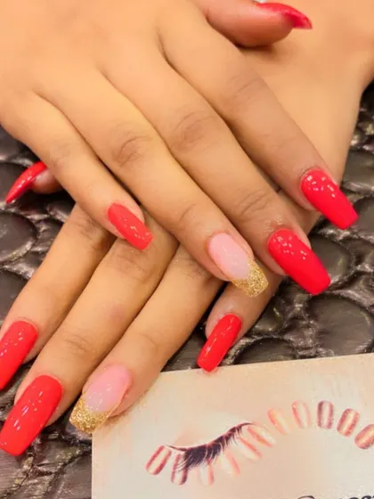 A vibrant set of long, square nails in a bright reddish-orange color. The ring fingers are accented with a gold glitter ombre at the base.