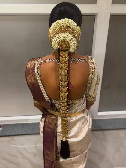 A stunning view of a traditional South Indian bridal hairstyle, complete with a full set of gold hair jewellery and a jasmine flower arrangement at the top.