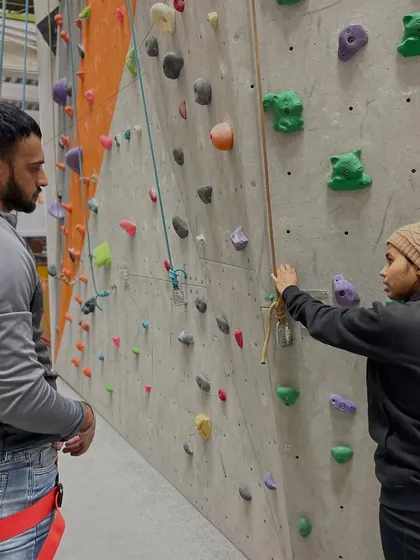 An instructor explains the basics of our auto belay system to a new climber. This system allows you to climb on your own and descend safely, making it perfect for practice.
