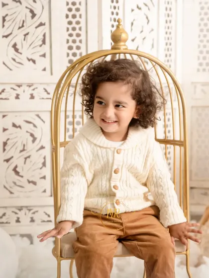 A candid shot of a smiling toddler seated in a stylish golden chair prop. My goal is to capture genuine expressions and playful moments.