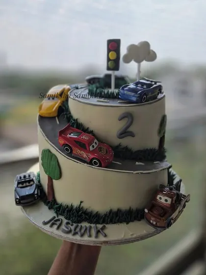 This car-themed cake features a winding road that spirals up two tiers, with favorite toy cars racing along the way. It's a playful and interactive design for any little vehicle enthusiast.