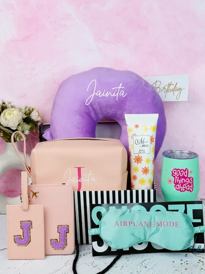 A closer look at the personalized birthday hamper. It includes a custom neck pillow, a monogrammed pouch and luggage tag, a fun tumbler, and a relaxing eye mask.