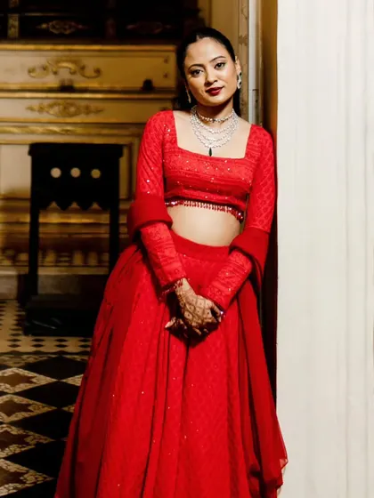 The bride posing in her vibrant red sangeet outfit. The sleek ponytail and glamorous makeup create a very chic and modern look.